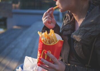 woman in brown classic trench coat eating mcdo fries during daytime