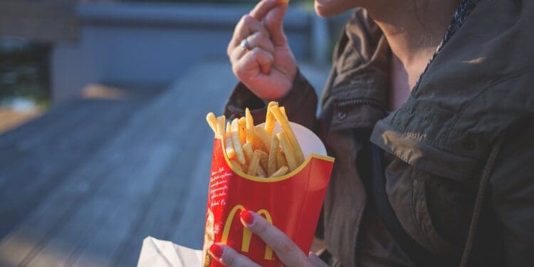 woman in brown classic trench coat eating mcdo fries during daytime