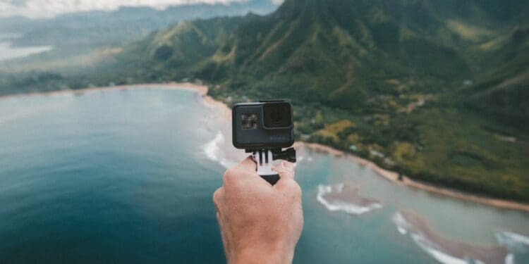 person holding black action camera fronting green mountains