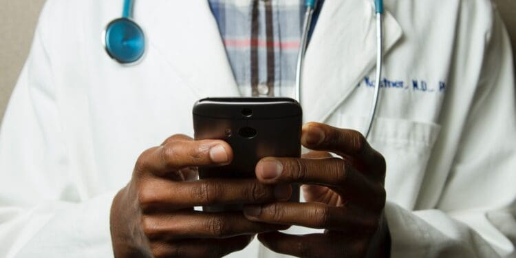 person wearing lavatory gown with green stethoscope on neck using phone while standing