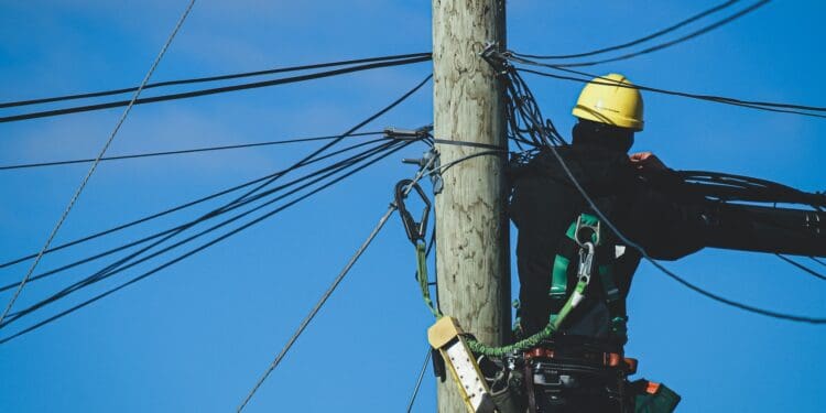 man in black jacket and yellow helmet on brown wooden post under blue sky during daytime