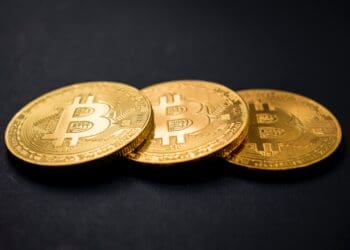 three gold-colored bitcoins on black surface