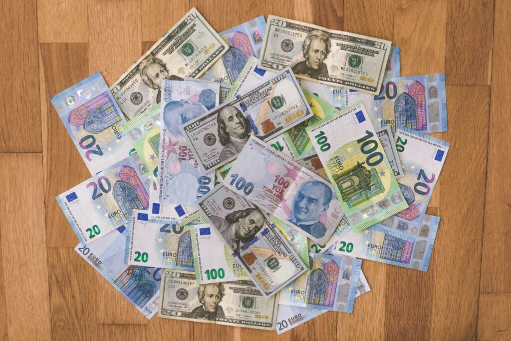 20, 100 Euro <noread>(EUR)</noread>, and 20, 100 Dollar <noread>(USD)</noread>, and 100 Turkish Lira <noread>(TRY)</noread> banknotes placed on a wooden surface.