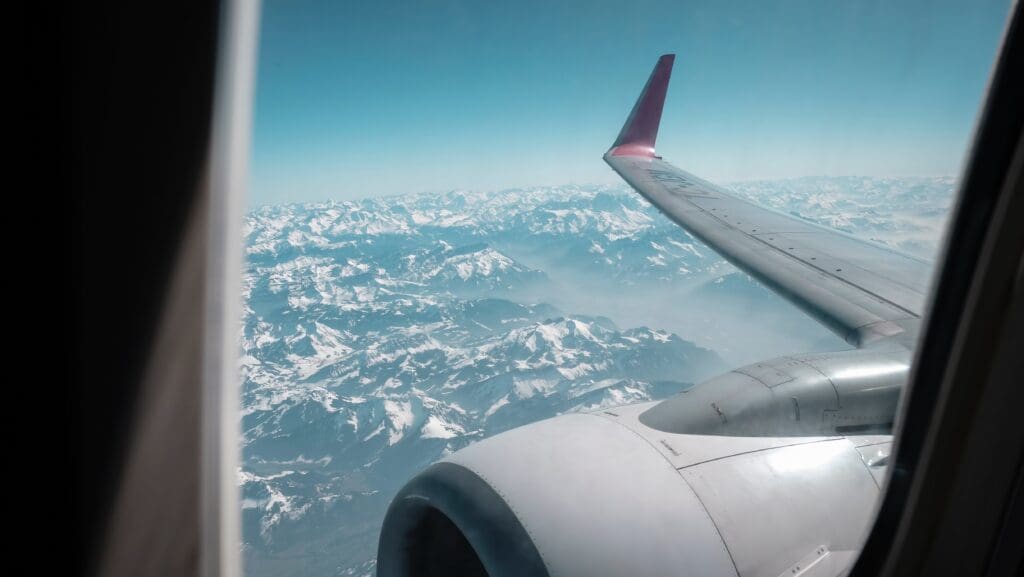 A plane's wing and motor seen from the window, above mountains.