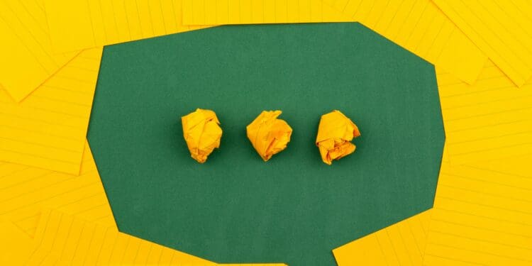orange sheets of paper lie on a green school board and form a chat bubble with three crumpled papers.
