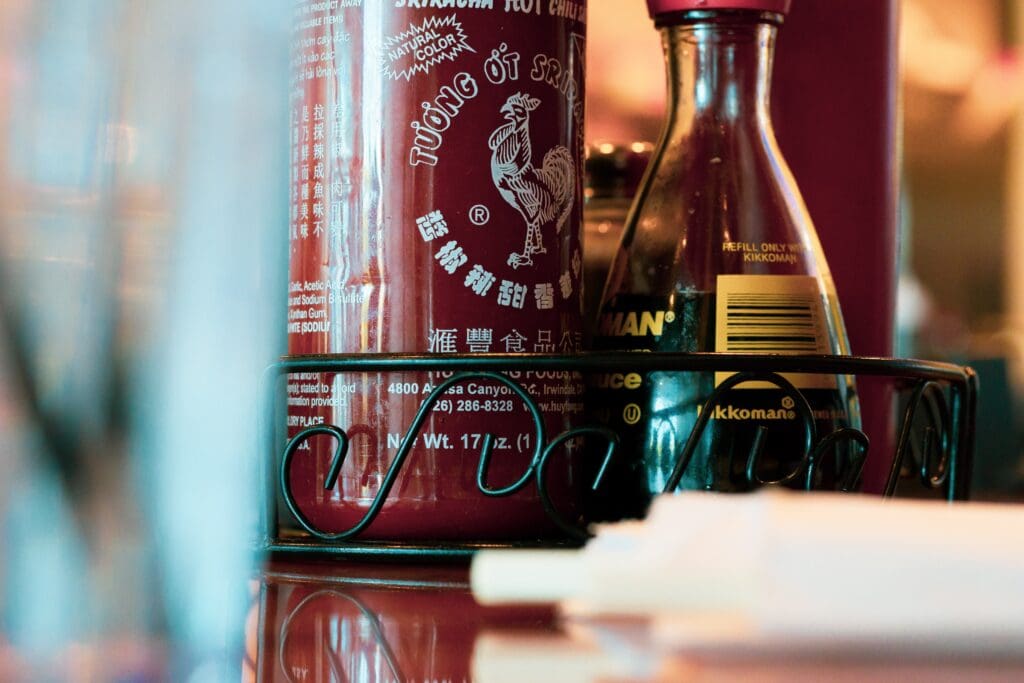 Photograph of a table in an Asian restaurant focusing on bottles of Sriracha Sauce and Soy Sauce.