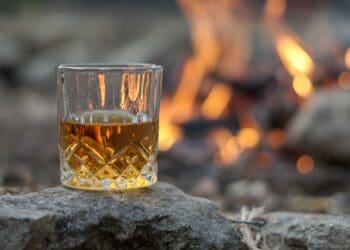 Vintage crystal glass of bourbon whiskey by an outdoor campfire