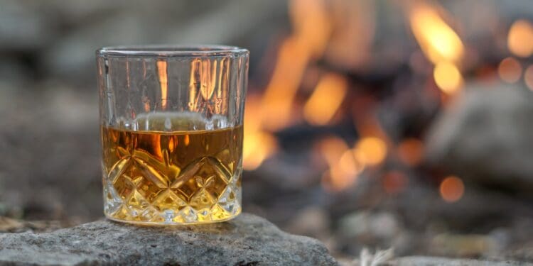 Vintage crystal glass of bourbon whiskey by an outdoor campfire