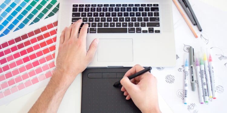 Graphic designer working on a Macbook laptop using a trackpad, color charts and markers