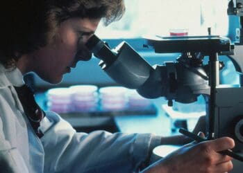 Profile shot of a Caucasian female scientist looking through an inverted microscope at cells that have been grown in culture media.