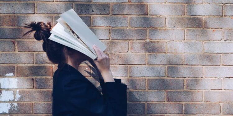 School Girl with Book in front of natural rustic red brick background holding book up to her face.