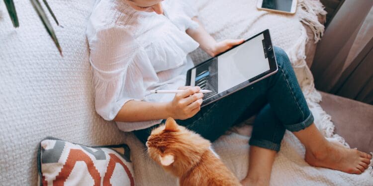 woman in white long sleeve shirt and blue denim shorts sitting on bed using tablet computer
