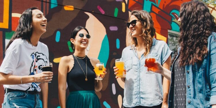 four women holding drinks while laughing together during daytime