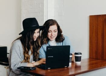 two woman sitting near table using Samsung laptop