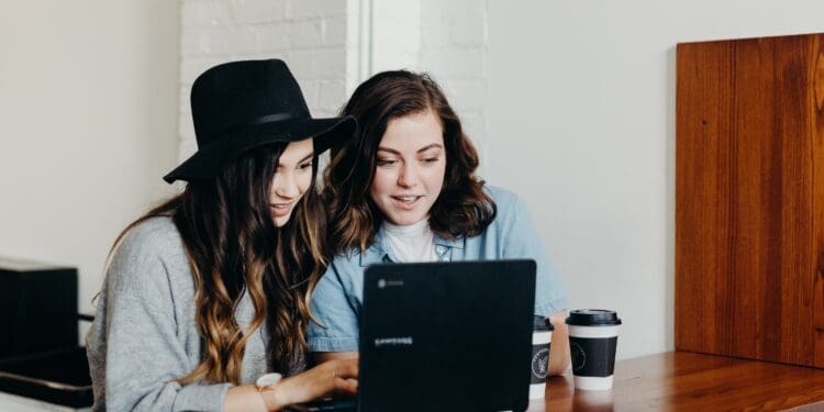 two woman sitting near table using Samsung laptop