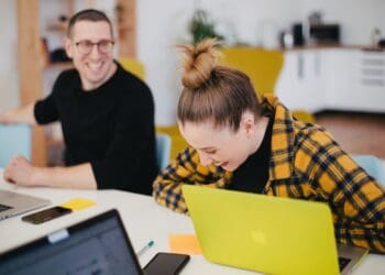 man and woman laughing while sitting in front of laptops