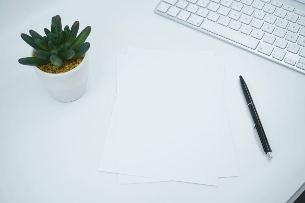 White papers lying on an office desk next to pen,keyboard and small pot flower. Great mockup shot for showcasing a document or print design