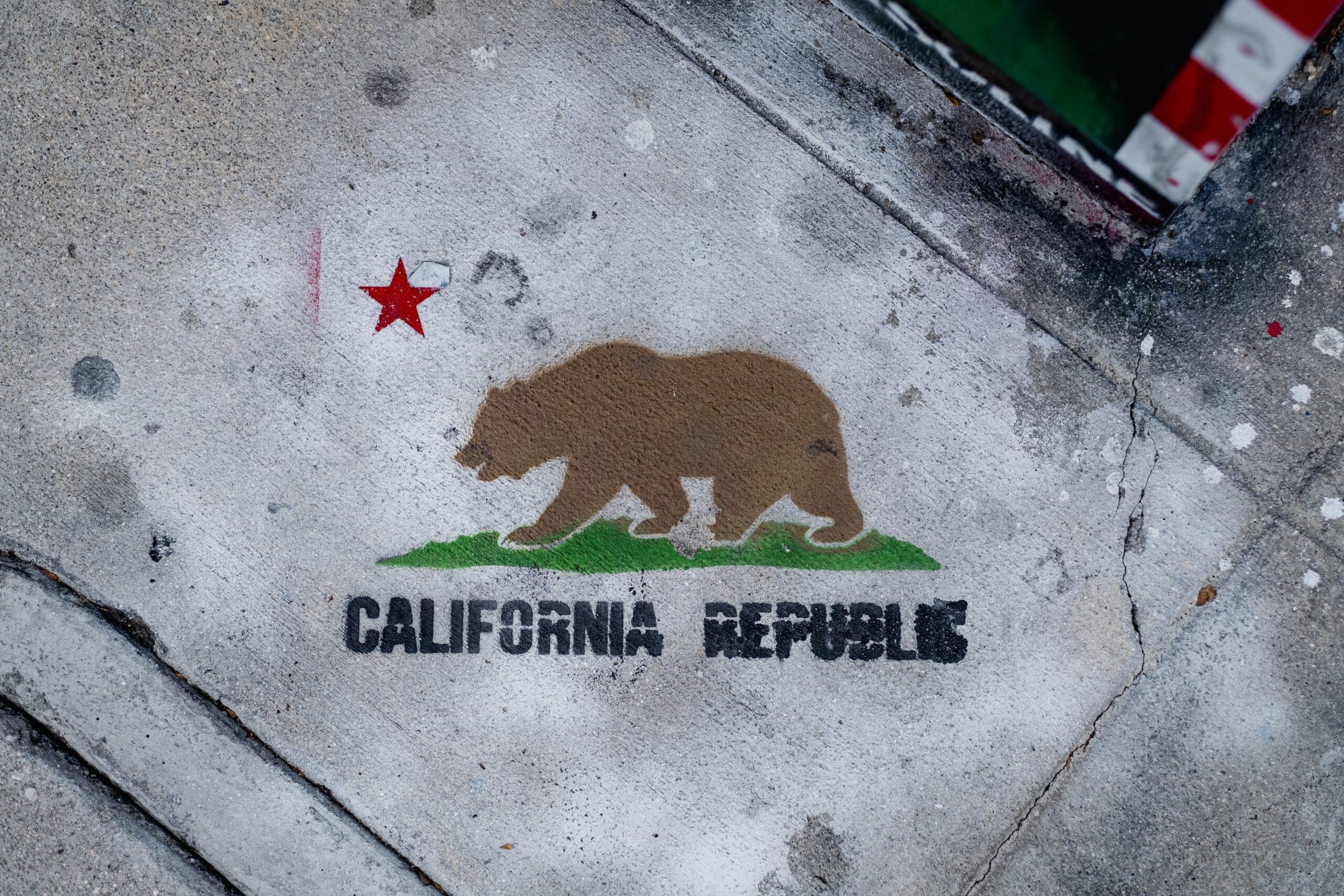 Stencil graffiti on the sidewalk, showing the flag of California.