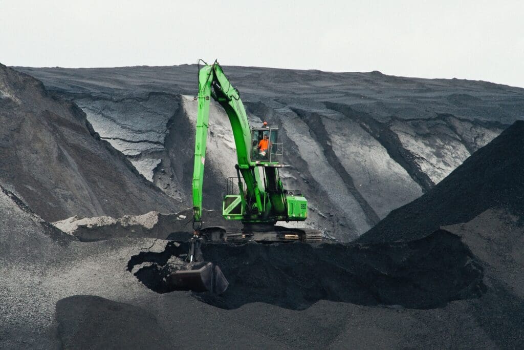 green backhoe digging hole in the middle of mountain