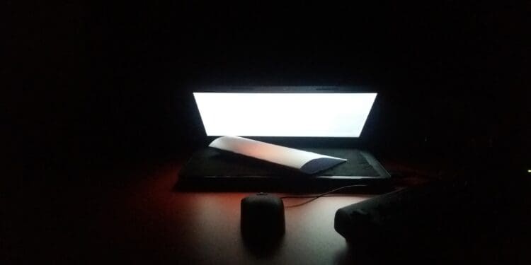 laptop in dark at night on table with mouse, lamp, paper.